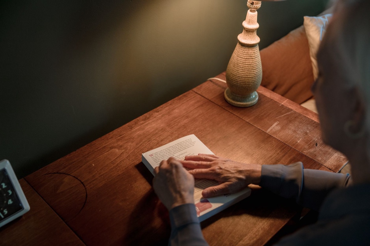 A person reading a book under a properly positioned desk lamp with soft light.