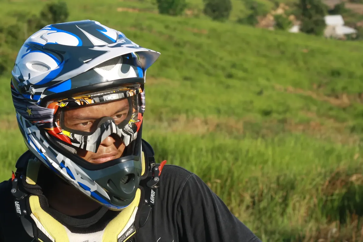 Dirt biker with colorful helmet looks determined in a grassy outdoor setting, ready for adventure.