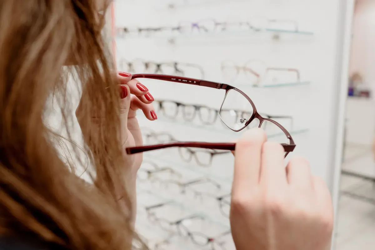 Crop anonymous female client choosing eyeglasses for treating eyes in optical salon with variety of choice