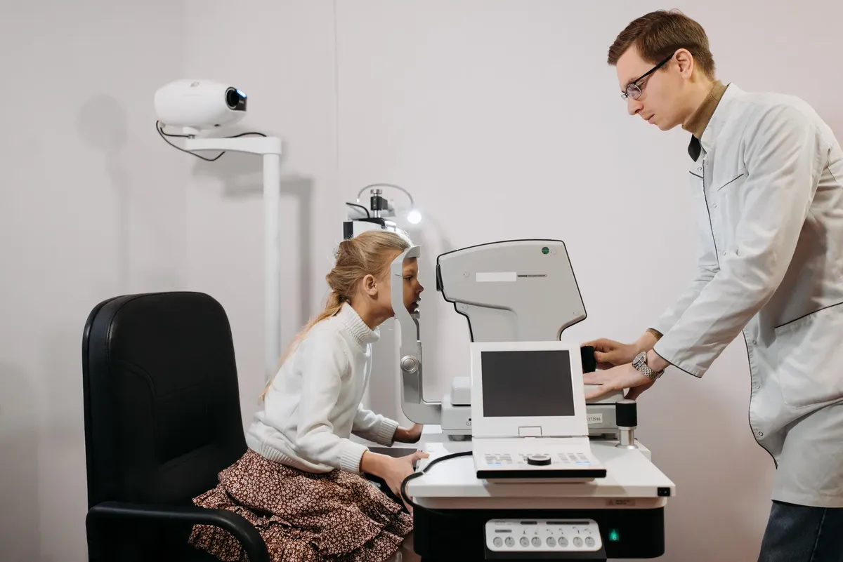 A young girl receives an eye exam from an optician in a clinical setting, focused on vision health.
