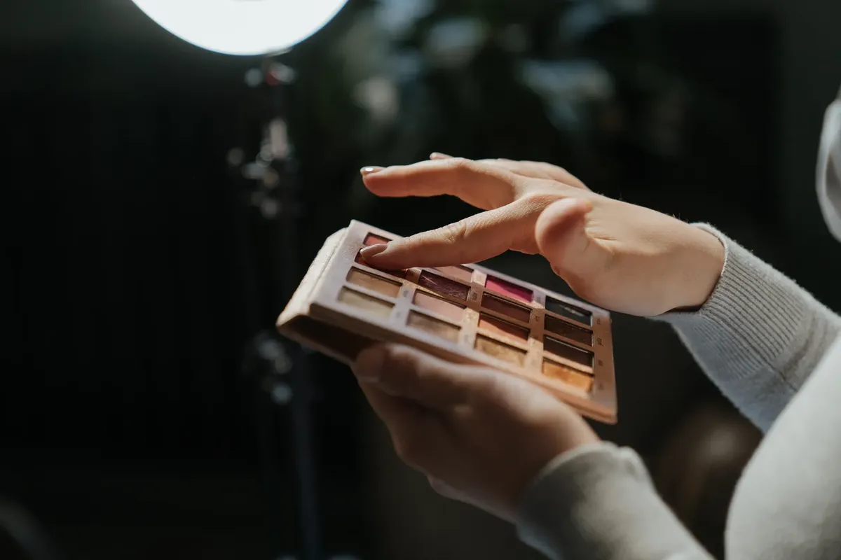 Hands applying eyeshadow from a palette under studio lighting.
