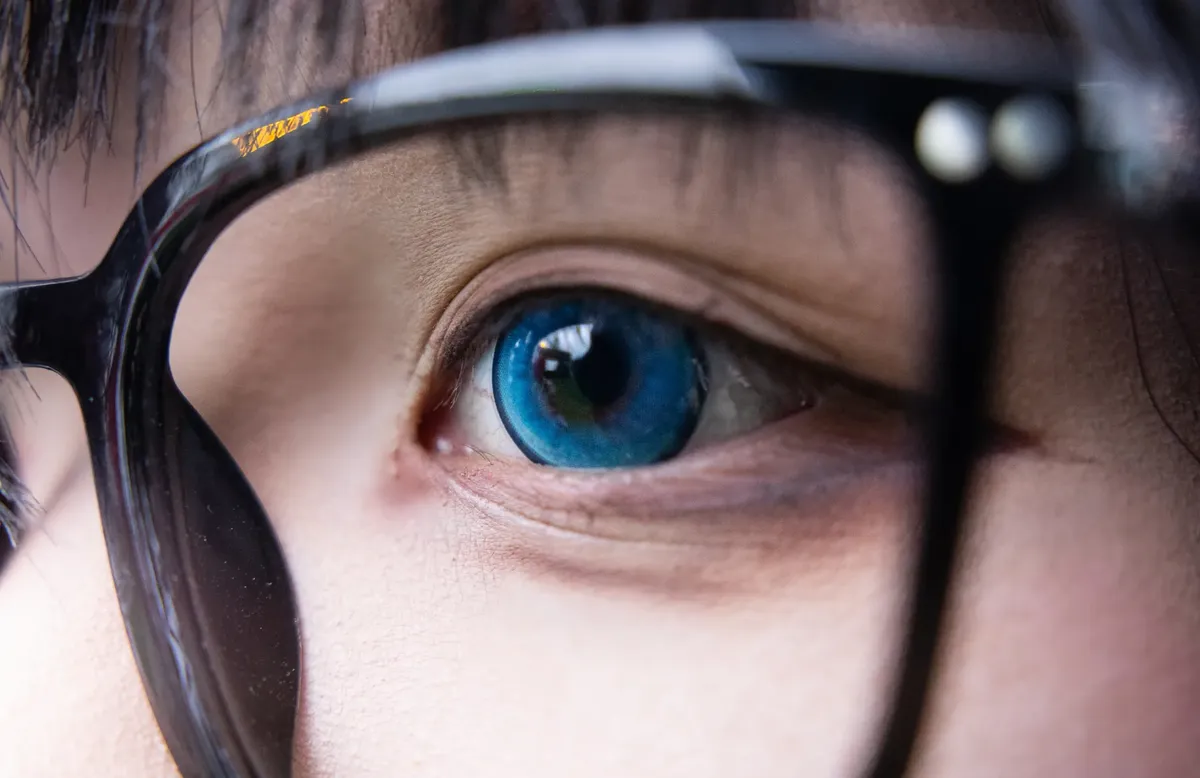 Detailed close-up image of an eye wearing blue contact lens and glasses, highlighting eye expression.