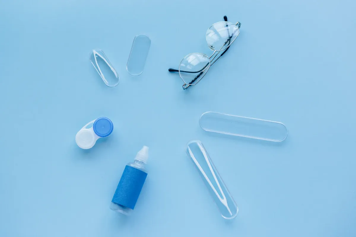 파란 배경 위에 접촉 렌즈 케이스, 용액, 그리고 안경의 평평한 레이아웃입니다.