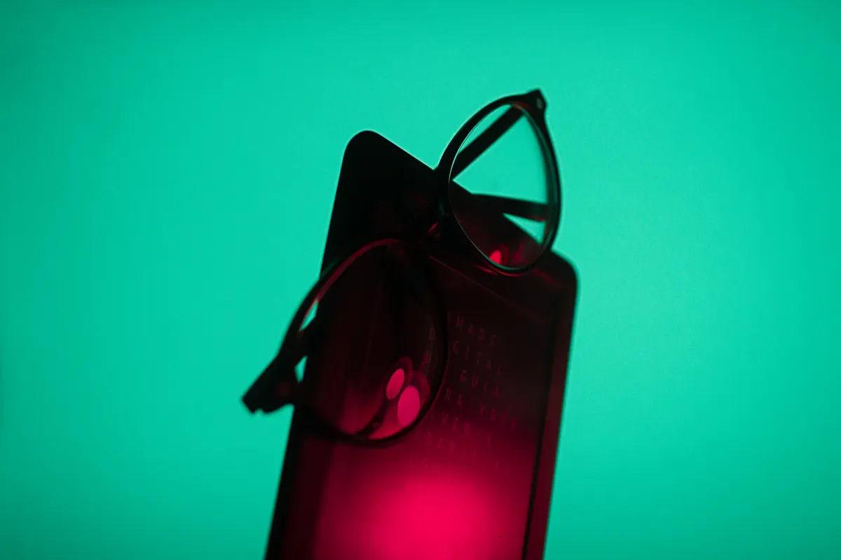 Stylish eyeglasses placed on a smartphone with a vibrant turquoise background.